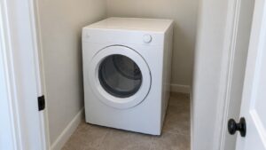 A compact white dryer standing in a narrow alcove with no duct behind it
